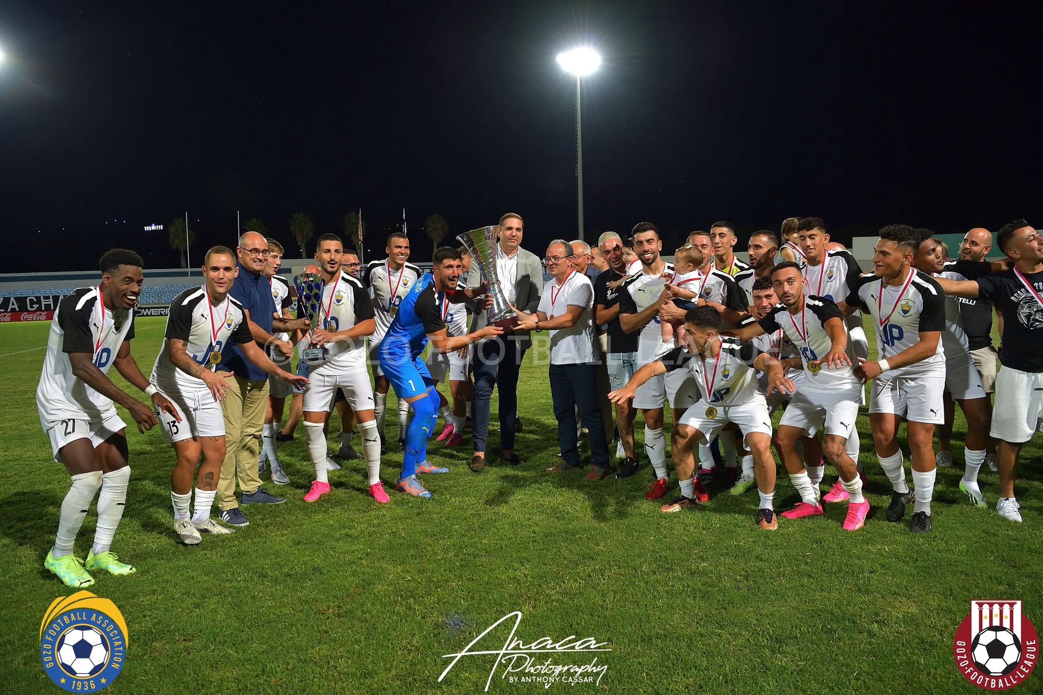 Nadur Youngsters squad celebrating with silverware under the floodlights